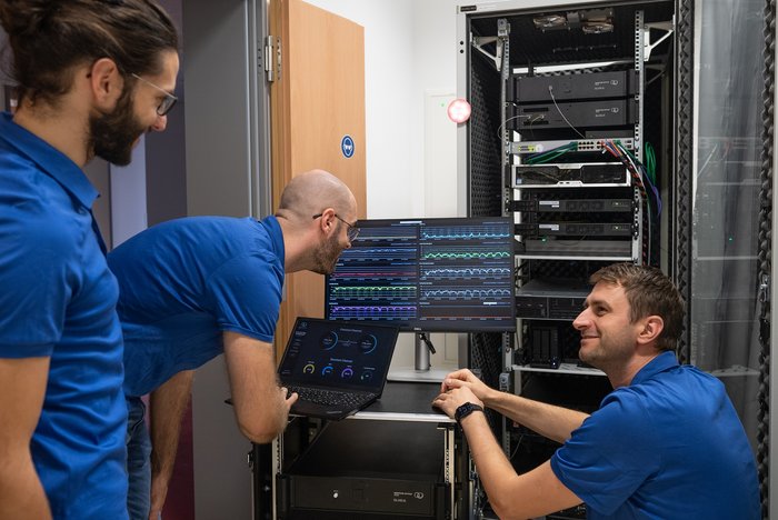 Team der Quantum Optics Jena GmbH Drei Männer in blauen T-Shirts an einer Art Schaltkasten