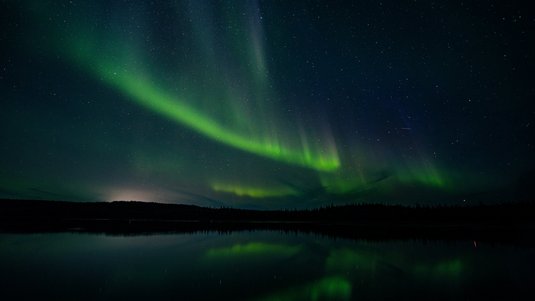 Über einem See sind am Nachthimmel grüne Polarlichter zu sehen.