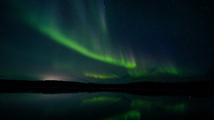 Über einem See sind am Nachthimmel grüne Polarlichter zu sehen.