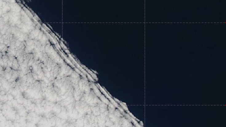 Satellitenaufnahme. Man erkennt Wolken mit einer scharf geschnittenen Kante über dem Meer. Rechts davon ist eine Küste zu sehen.