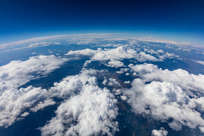 Blick von außen auf die Erde. Über Land und Meer befinden sich Wolken.