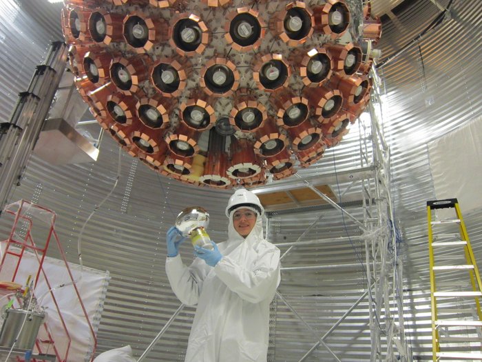 Eine Wissenschaftlerin baut ein Bauteil in einen großen kugelförmigen Detektor ein.