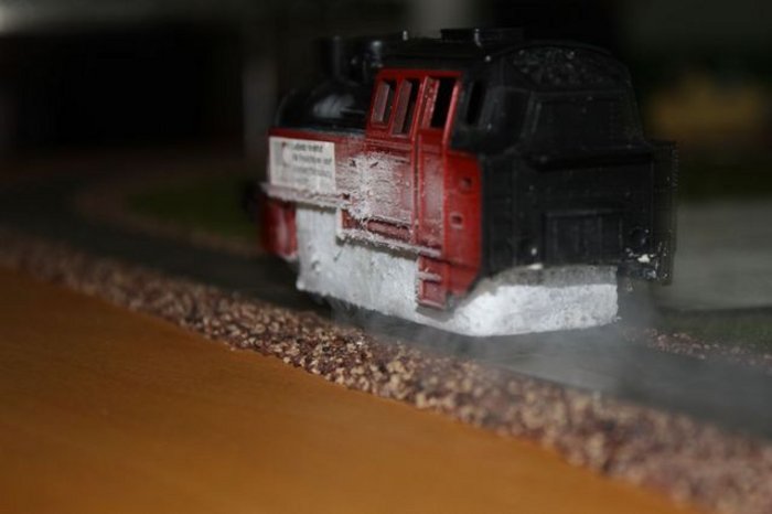 Foto: Schwarze Spielzeug-Lokomotive ohne Räder schwebt dicht über den Schienen, dazwischen etwas Dampf.