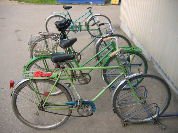 Das gleiche in grün: Fahrräder sehen immer ungefähr gleich aus Vier unterschiedliche, alte Fahrräder stehen in einem Fahrradständer. Sie unterschieden sich in Details, zum Beispiel in der Anordnung der Stangen des Rahmens.