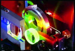 Foto: Experiment, von in Spektralfarben zerlegtem Licht beleuchtete Metallringe und Linsen