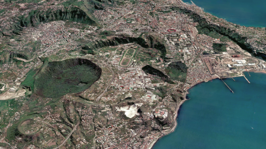 Das Bild zeigt die Phlegräischen Felder in der Nähe von Neapel. Die Caldera hat verschiedene Krater. Man sieht die Gebäude und Infrastruktur der Gemeinden, die in diesem Gebiet angesiedelt sind.
