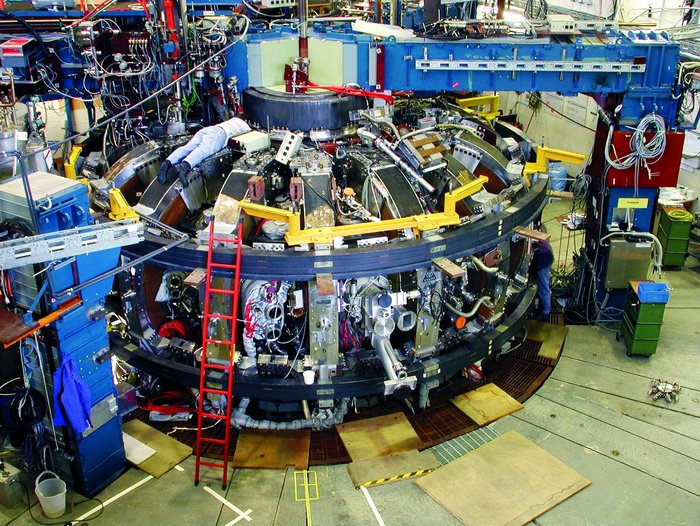 Das Fusionsexperiment TEXTOR-94 in Jülich ist ein kleiner Tokamak Seitenansicht des rund vier Meter hohen Textor-94: Die teilweise geöffnete Außenwand zeigt das Äußere des inneren Ringes. Davor ein messender Forscher im weißen Overall.