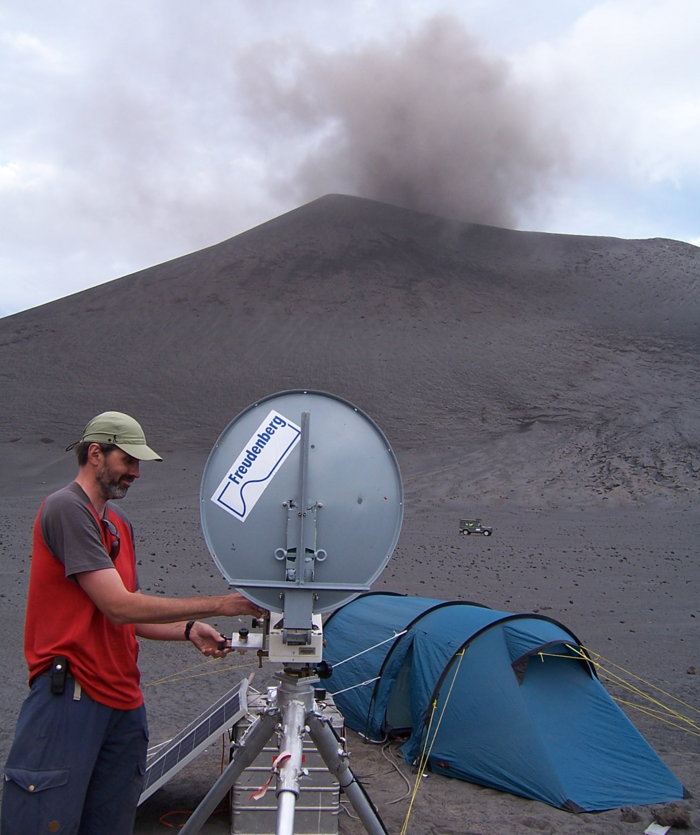 Matthias Hort am Vulkan Yasur Das Bild zeigt den Geophysiker vor einem Vulkan. Am Fuß des Vulkans stehen ein Auto und ein aufgebautes Zelt.