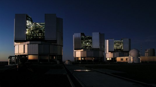 Das Foto zeigt drei geöffnete Teleskopkuppeln bei Nacht.