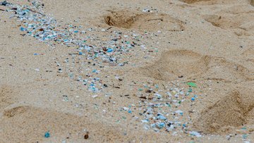 Die Nahaufnahme zeigt feinen Sand. Darauf sind unzählige kleine Plastikteile verstreut.