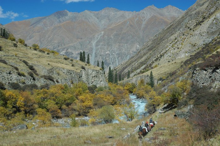 Tianshan Gebirge Gebirgskette, im Vordergrund ist ein Taleinschnitt mit einer Reisegruppe zu sehen.