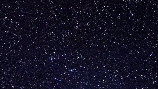 Sterne, davon einige hellere, die in einem Haufen geballt sind. Sie sind von Staub und Gas umgeben.