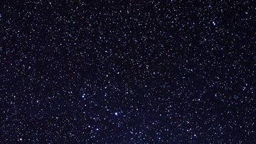 Sterne, davon einige hellere, die in einem Haufen geballt sind. Sie sind von Staub und Gas umgeben.