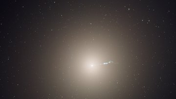 Große sphärische Galaxie hinter Sternen-Vordergrund. Vom Zentrum der Galaxie geht ein Strahl aus.