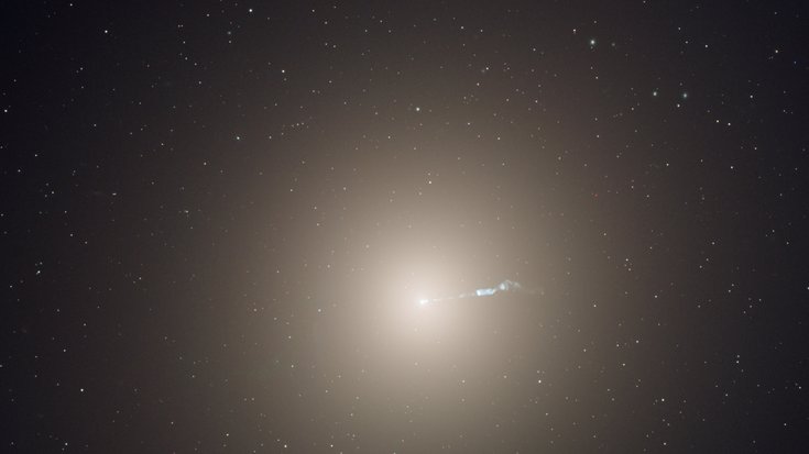 Große sphärische Galaxie hinter Sternen-Vordergrund. Vom Zentrum der Galaxie geht ein Strahl aus.