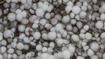 Foto. Viele Hagelkörner liegen auf dem Boden.