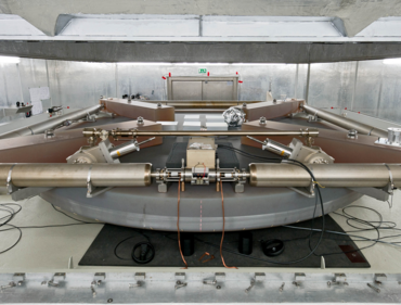 Metallische Scheibe in einem Raum mit Betondecke, auf dem sich röhrenartige maschinelle Aufbauten befinden