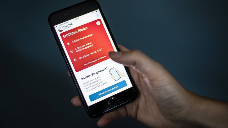 Ein Smartphone in einer Hand zeigt die Corona-Warn-App mit einem erhöhten Risiko an.