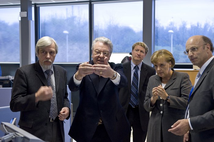Personen, die auf etwas außerhalb des Bildes schauen. Unter ihnen der CERN-Generaldirektor Rolf-Dieter Heuer und die deutsche Bundeskanzlerin Angela Merkel.