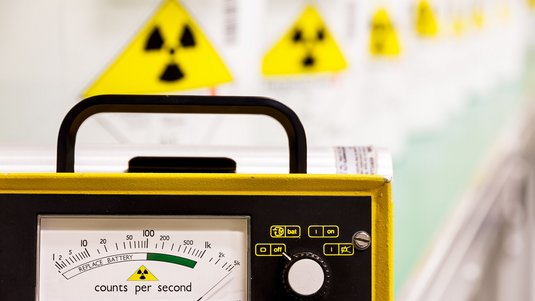 Das Foto zeigt ein Strahlungsmessgerät, im Hintergrund sind Behälter mit radioaktiven Stoffen zu erkennen