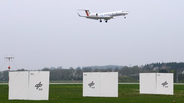 Das Bild zeigt den Rasenbereich vor einer Landebahn an einem kleinen Forschungsflughafen. Auf der Rasenfläche sind hochkant Sperrholzplatten angebracht.