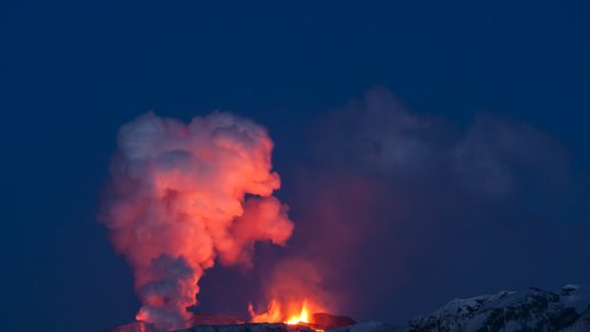 Das Bild zeigt einen Ausbruch des Eyjafjallajökull auf Island. Über der sehr hellen Lava im Krater hat sich eine Wolke gebildet. 