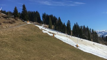 Berglandschaft: Eine Hälfte eines Berges ist mit Schnee bedeckt, auf dem Skifahrer fahren; die andere Hälfte ist unbeschneit