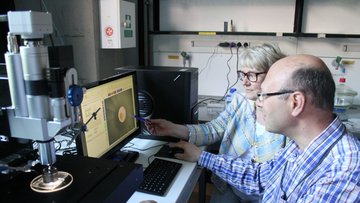 Zwei Forscher sitzen neben dem Mikromanipulator und vor einem Computer.