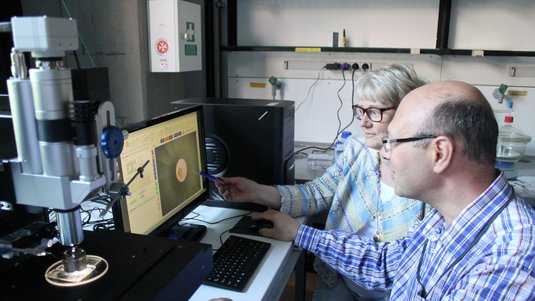 Zwei Forscher sitzen neben dem Mikromanipulator und vor einem Computer.