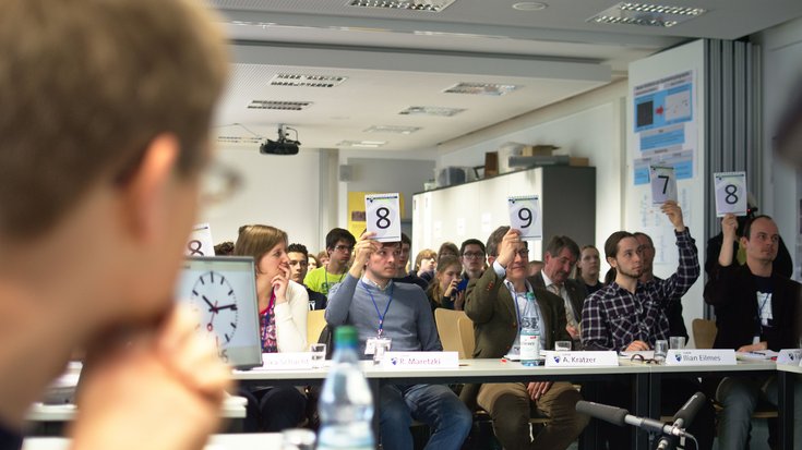 Juroren halten Wertungsschilder in die Höhe, neben ihnen eine große Uhr.