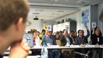 Juroren halten Wertungsschilder in die Höhe, neben ihnen eine große Uhr.