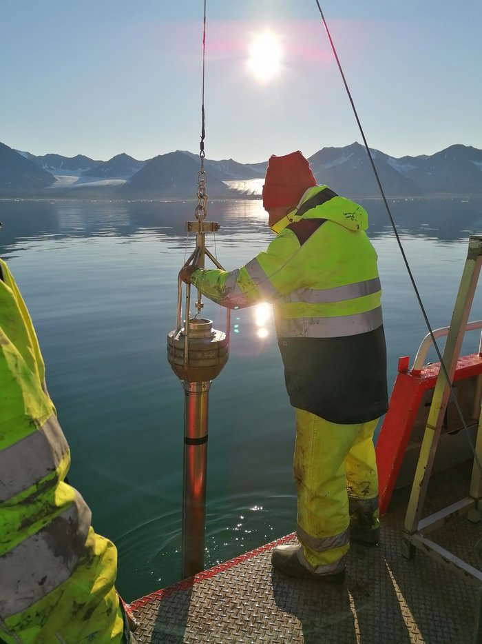 Klimaforschung in der Arktis Ein Arbeiter auf einem Schiff hält ein Rohr, dass an einem Stahlseil befestigt ist, ins Meer.