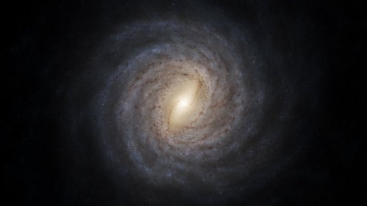 Spiralgalaxie von oben auf schwarzem Hintergrund. Heller Balken in der Mitte, von dem schwächer leuchtende Spiralarme aus gehen.