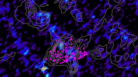 Ausschnitt der Molekülwolke, die Strahlungsintensität ist falrbig kodiert, Kontourlinien zeigen die Geschwindigkiet des gases im Inneren der Wolke. Ein Kreuz markiert eine kompakte Strahlungsquelle im Inneren der Wolke.