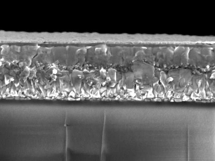 Mikroskopaufnahme der Solarzelle Schwarz-weiße Mikroskopaufnahme, auf der oben eine bröckelige Schicht und darunter ein glatte abgebildet sind