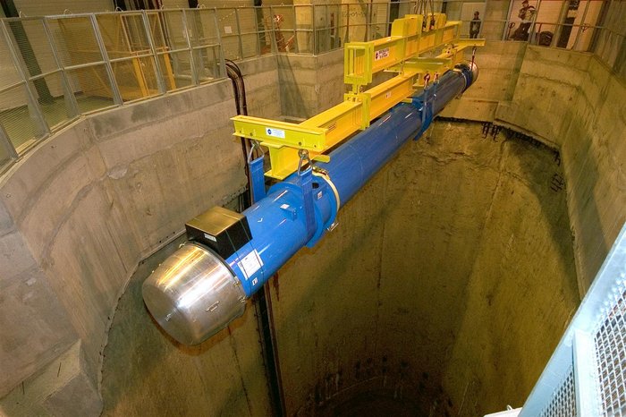 Der erste Hauptdipolmagnet wird herabgelassen Ein blau-silbernes riesiges Bauteil schwebt in einem Betonschacht an einem gelben Kran.