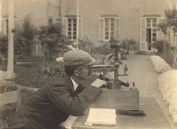 Historische Fotografie von Pacini in einem Garten, während er durch das Rohr eines Messgeräts schaut, das auf einem Tisch steht.