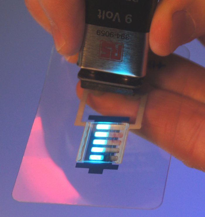 Ein OLED wird mit einer Batterie als Spannungsquelle zum Leuchten angeregt. Die OLED-Schichten können prinzipiell auch in einem modifizierten Tintenstrahldruckverfahren oder auch im Offsetdruck hergestellt werden. Das verspricht ein zukünftiges kostengünstiges Herstellungsverfahren, da andere Beleuchtungstechniken oft nur unter teuren Reinraum-Bedingungen hergestellt werden können.