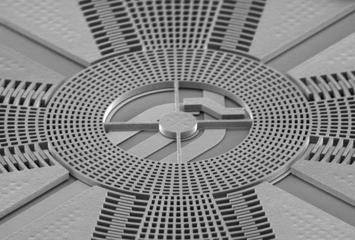 Drehratensensor in Mikrosystemtechnik Mikroskopaufnahme: Ein Kreis mit Riffelstruktur geht links und rechts in eine Art halbrunden Seitenstreifen über, zusammen formt sich so fast ein Oval; an den vier "Ecken" sind Rillenstrukturen sichtbar.