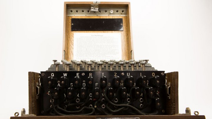 Eine altertümlich wirkende Schreibmaschine mit zahlreichen Anschlüssen für Kabel, die mit Buchstaben markiert sind.
