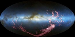 Waagerecht durch das Bild zieht sich die Milchstraße, rechts darunter zwei helle ausgedehnte Objekte, von denen ein langes Band nach links ausgeht.
