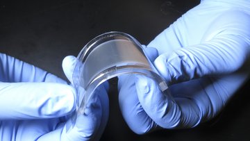 Zwei behandschuhte Hände biegen ein Modul aus Kunststoff, dass außen transparent und innen milchig ist.