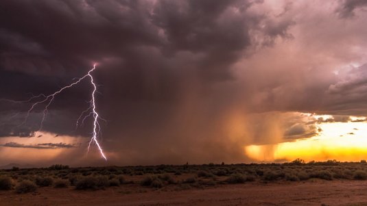 Dunkle Wolken und Blitze über einer Wüstenlandschaft