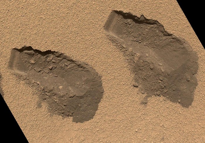 Zwei Furchen von etwa vier Zentimeter Breite in rötlichem Sand.