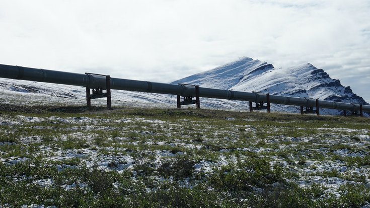 Eine Rohrleitung verläuft durch eine leicht schneebedeckte Landschaft, im Hintergrund Berge
