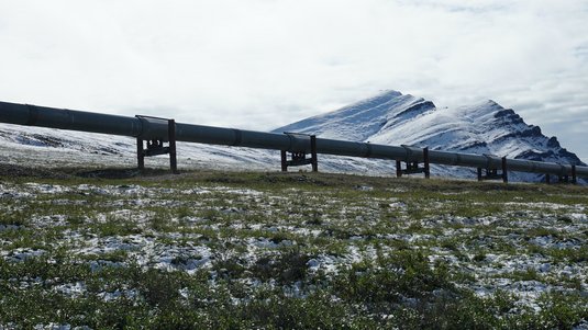 Eine Rohrleitung verläuft durch eine leicht schneebedeckte Landschaft, im Hintergrund Berge