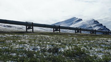 Eine Rohrleitung verläuft durch eine leicht schneebedeckte Landschaft, im Hintergrund Berge
