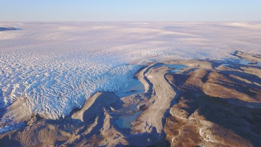 Luftaufnahme von Grönland: Ein Gletscher grenzt an grauer Felslandschaft