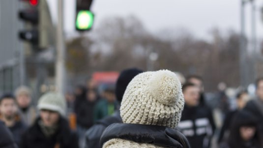 Rückansicht einer Person mit Mütze an einer grünen Ampel