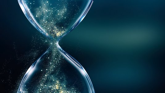 Auf dem Bild ist eine Sanduhr aus Glas abgebildet. Anstelle von Sand rieseln leuchtende Partikel von der oberen in die untere Hälfte.